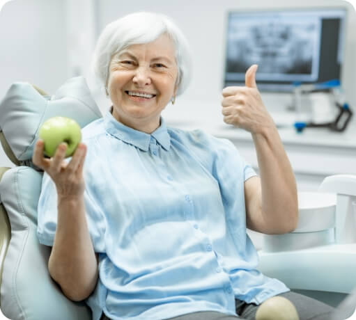 Smiling woman with dentures eating an apple