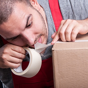 Man using his teeth to cut tape on box