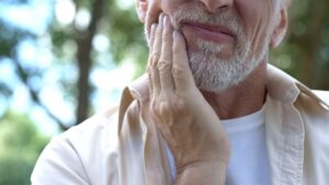Older man holding jaw in pain.